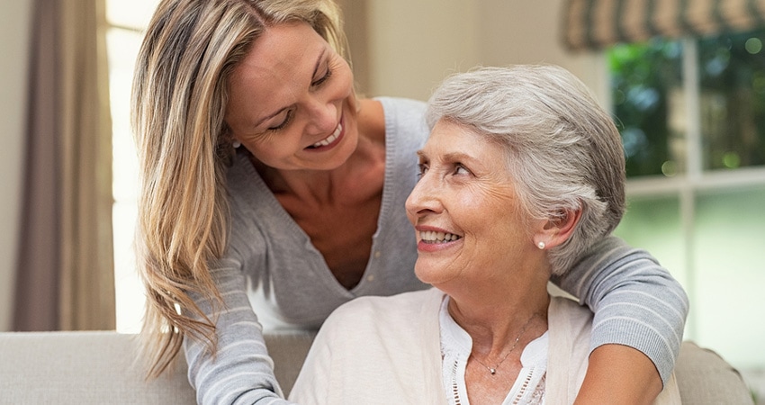 Portrait of mother and mature daughter hugging at home. Happ